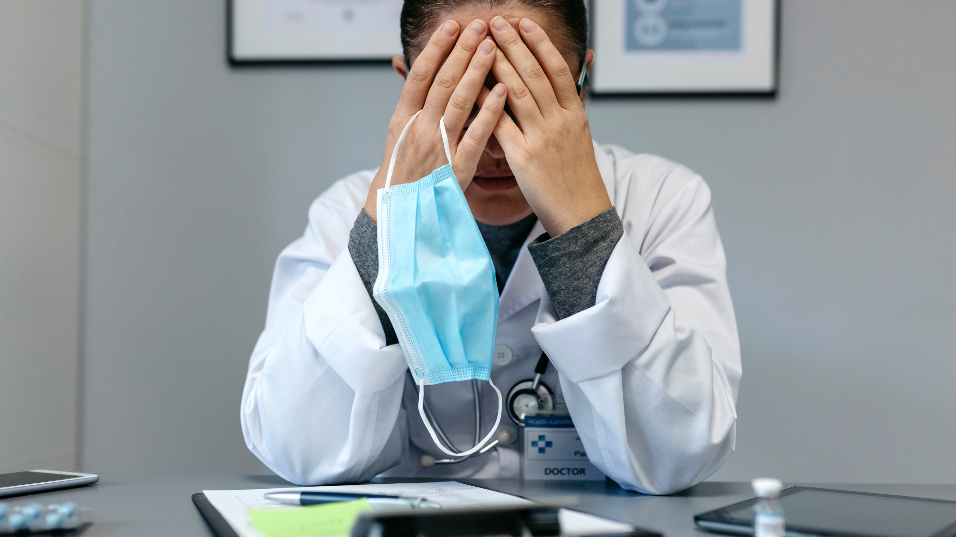 Doctor experiencing burnout sitting at desk showing stress with their hands on their face