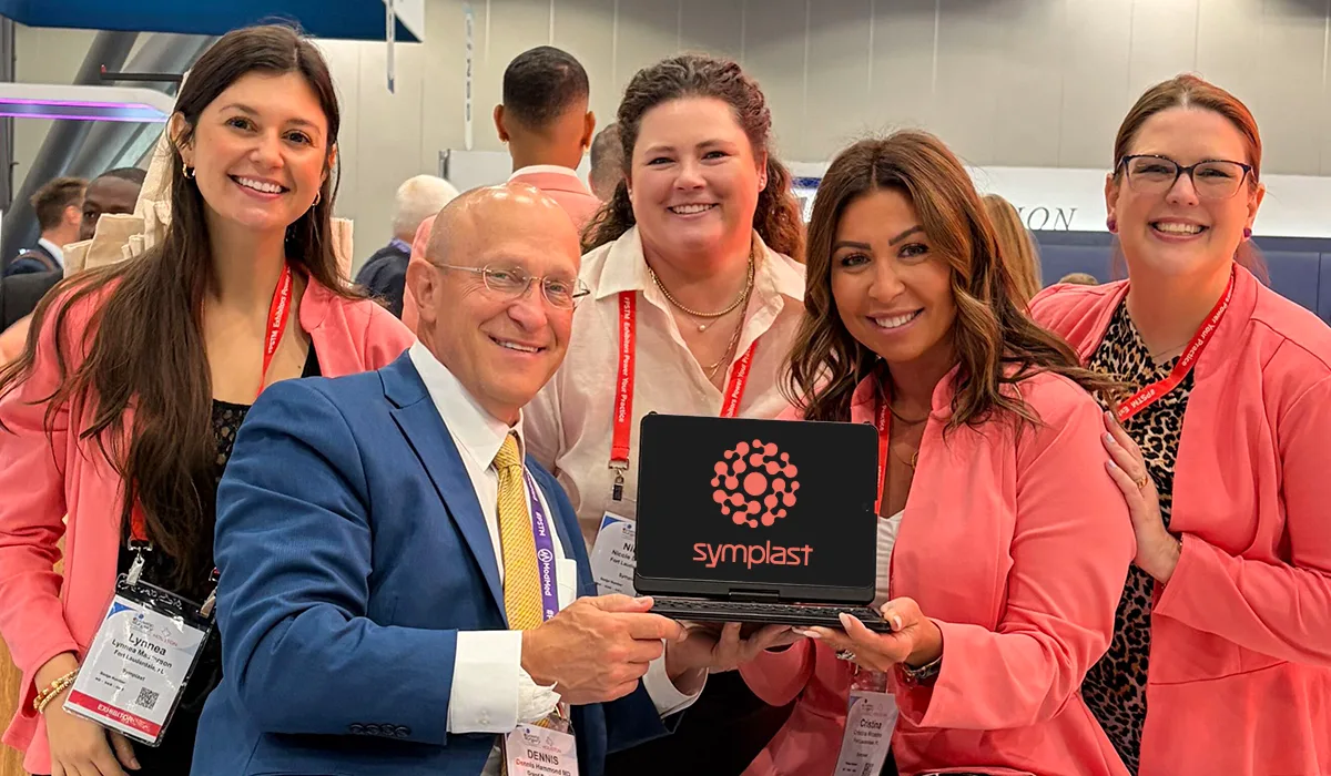 Symplast team members smiling at the PSTM 2026 booth, holding a tablet showing the Symplast logo